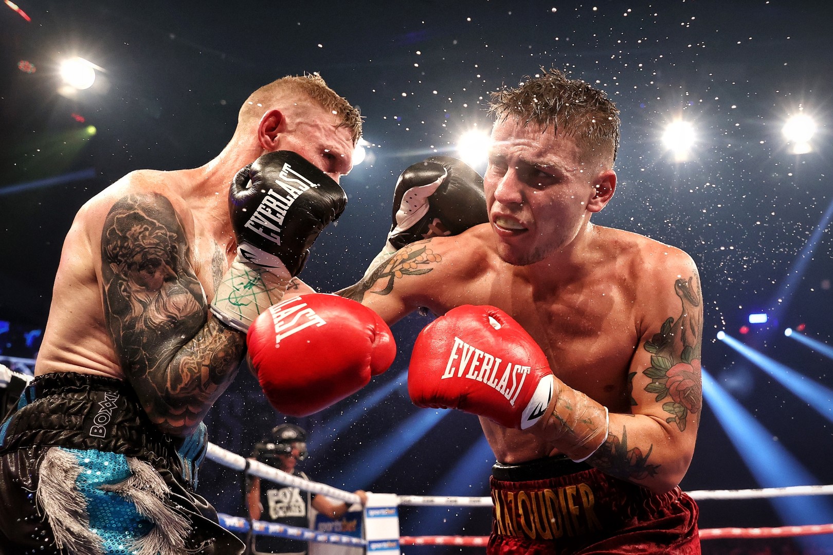Two male boxers with tattoos fighting in the ring underneath bright lights.