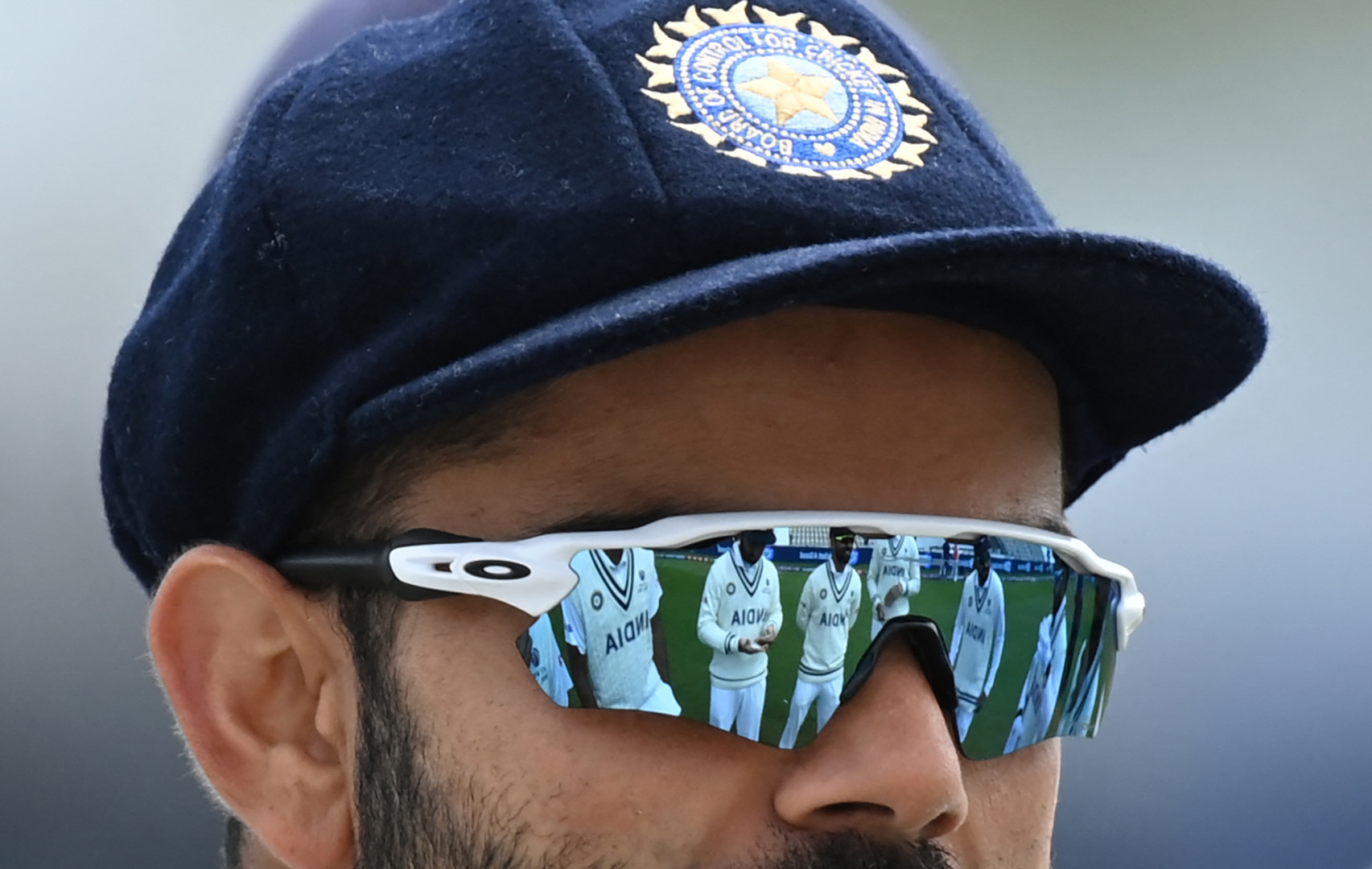 Close up head shot of cricket player's glasses reflecting his other teammates. 