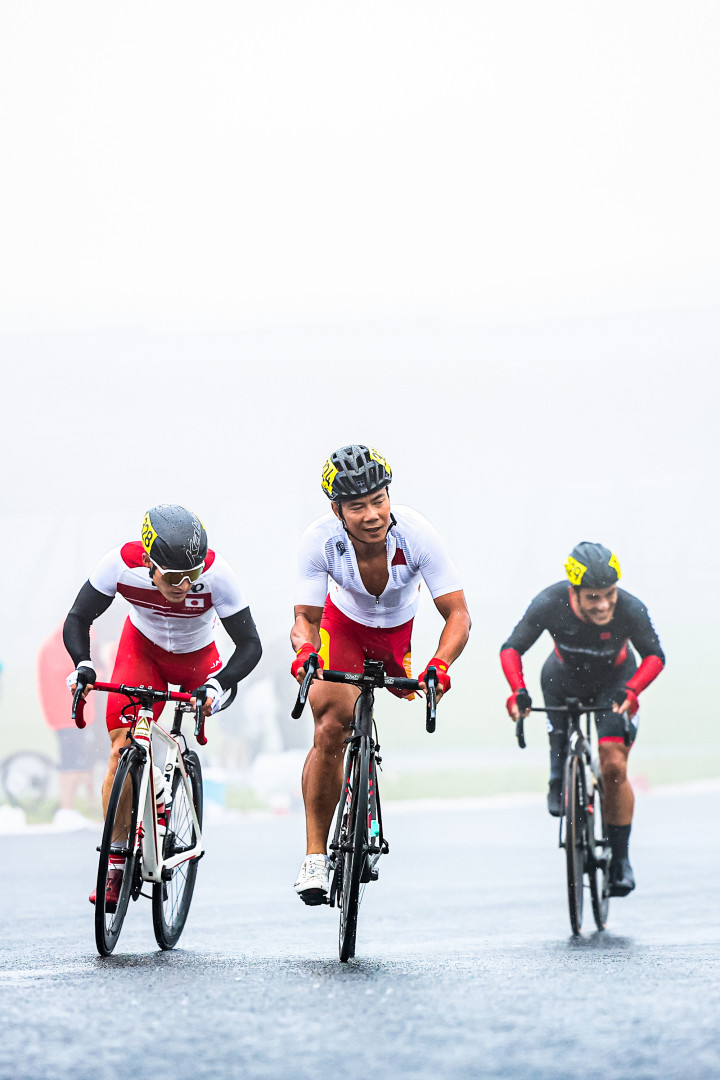 Three Paralympic road cyclists riding through foggy conditions.