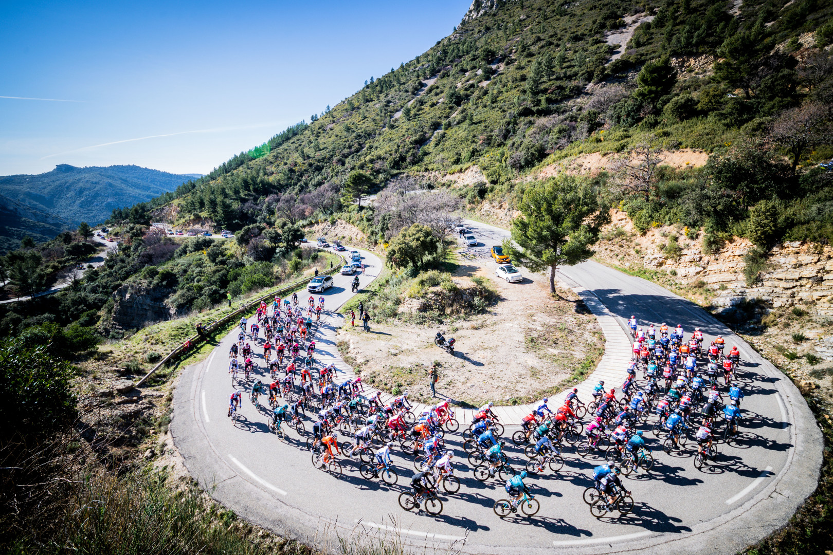 Cyclists riding up hill, around a bend, in the Tour de la Provence.