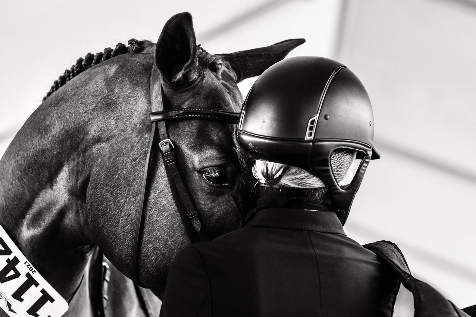 Close up black & white photograph of a horse and it's jockey resting their heads on each other.