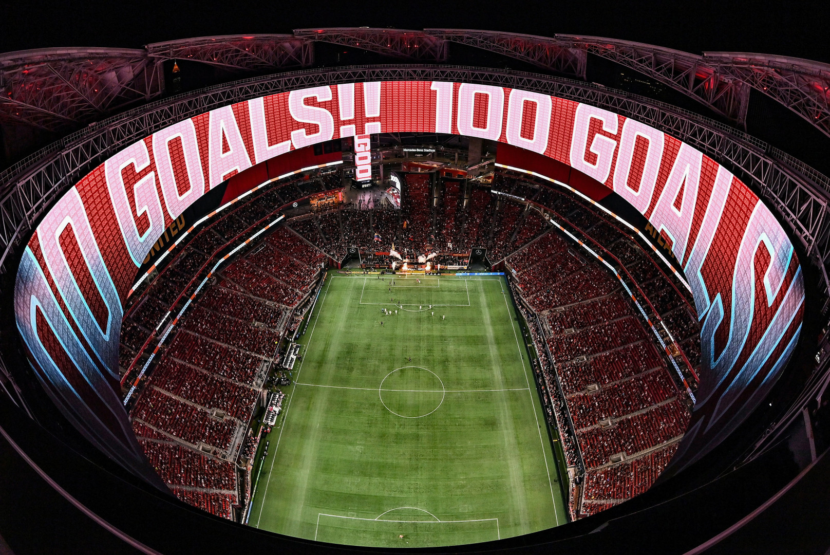 Aerial photograph off football stadium full of people, lit up in red.