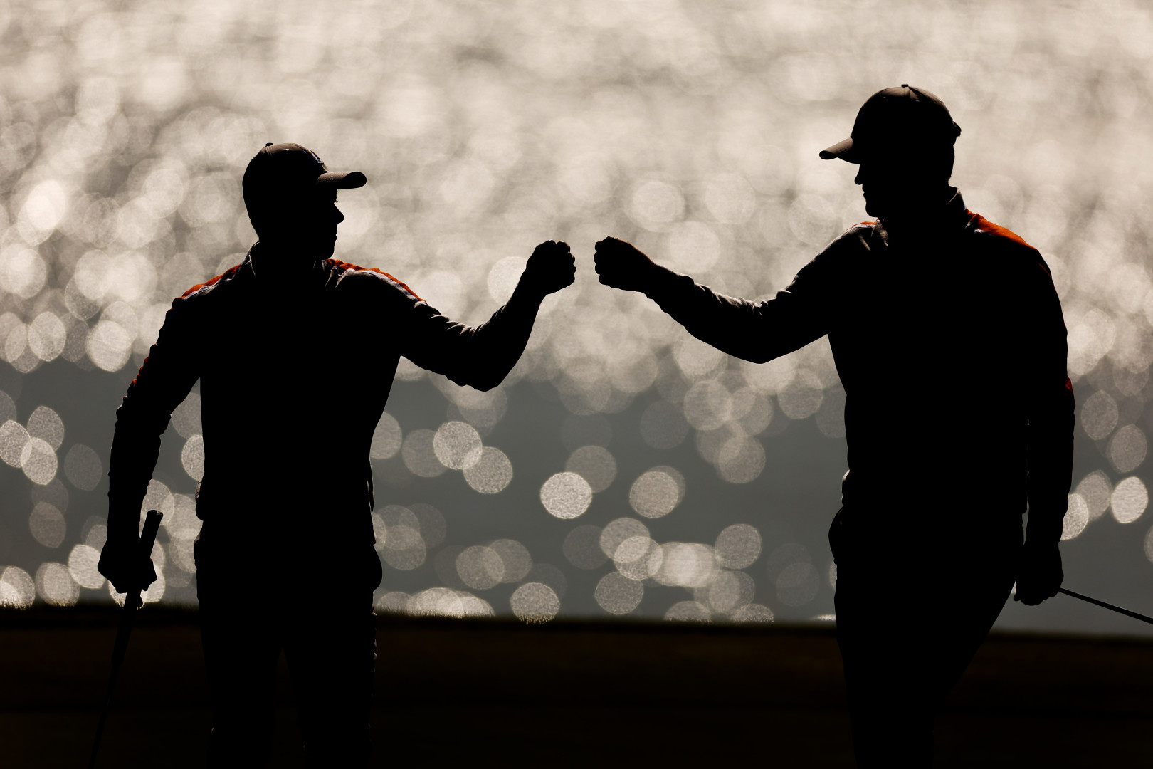 Two golfers bumping fists as the water of the lake glistens in the background.