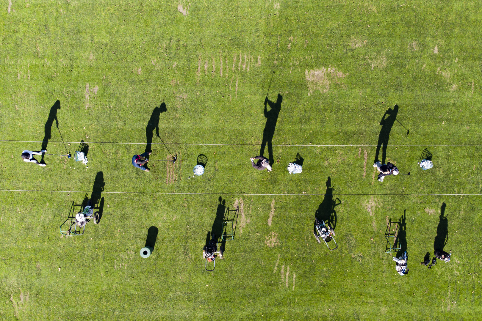 Birdseye view photograph of four golfers making their shots as their shadows reflect onto the green.