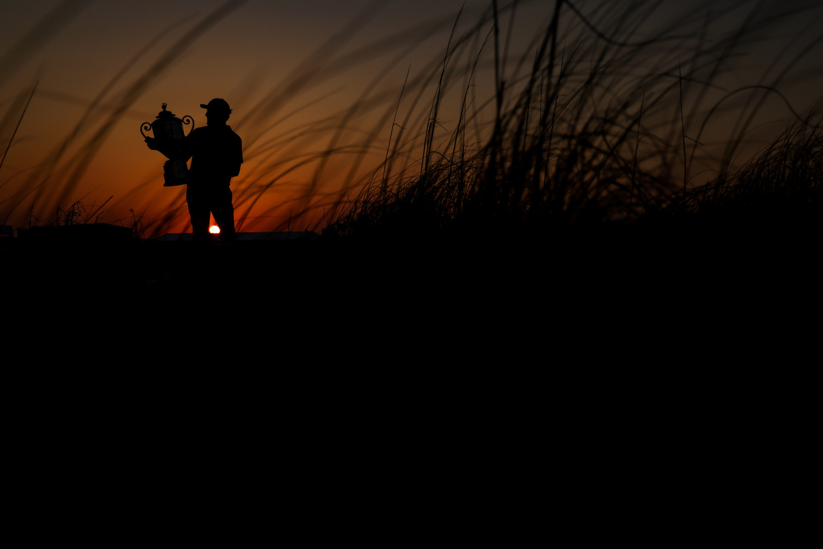 Silhouette of golfer holding the winning trophy in front of a sunset background.