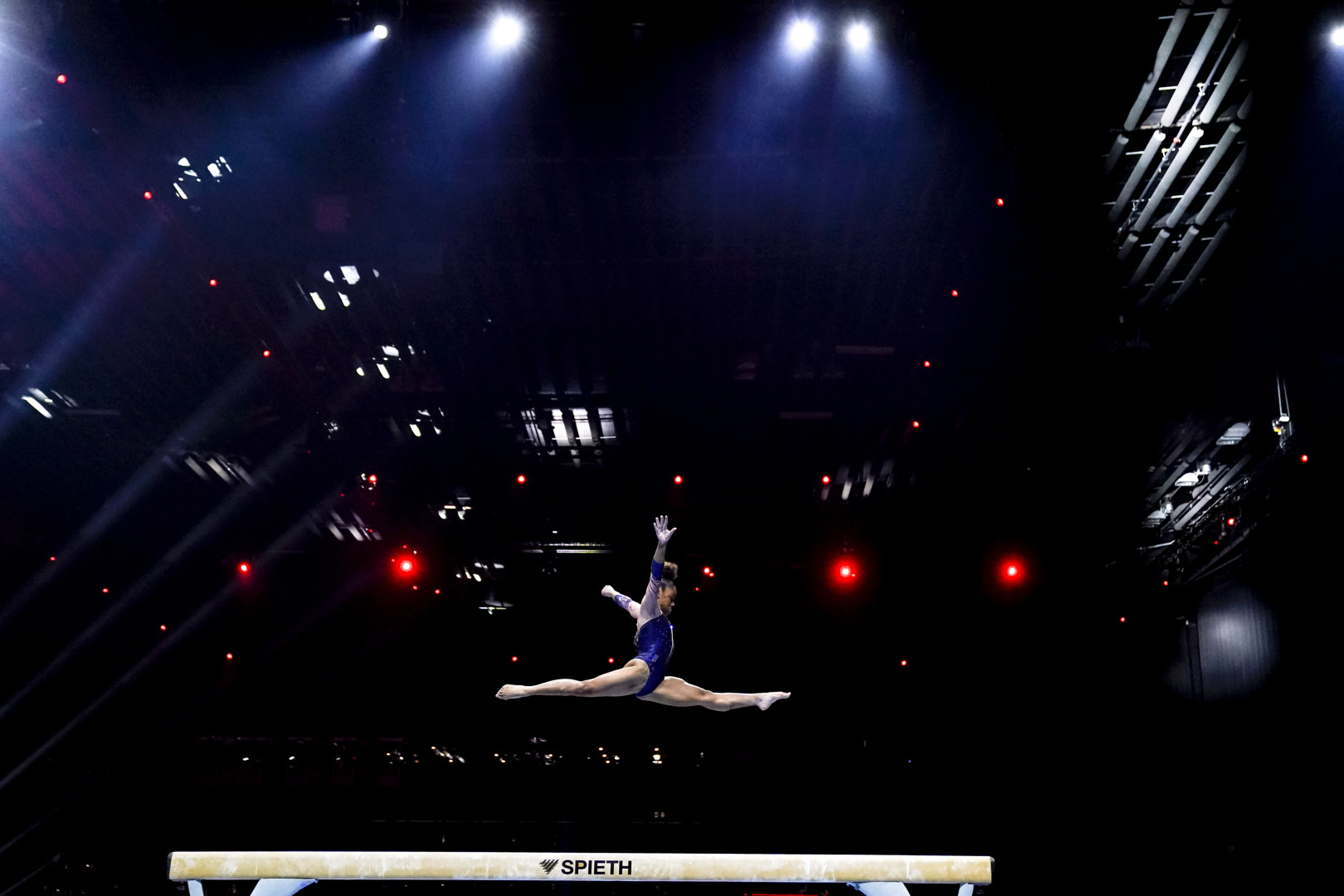 Side on photograph of a gymnast in a split jump over the beam.