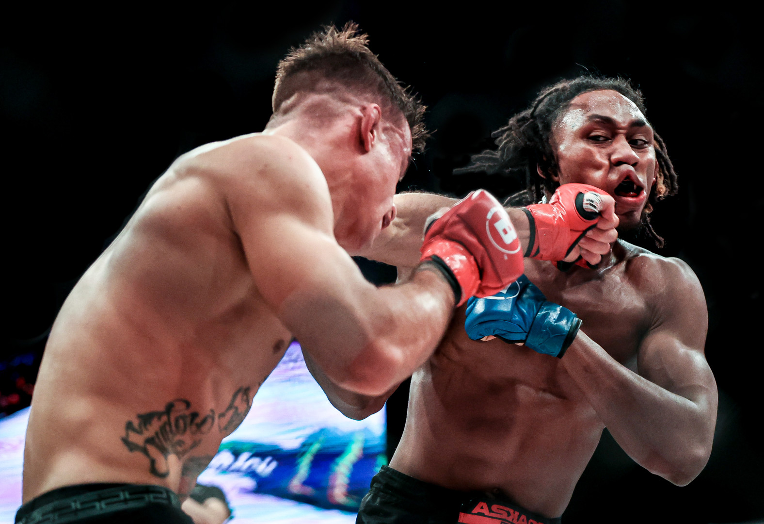 Two kickboxers in the ring as one gives the other a left hook, narrowly missing his lip.