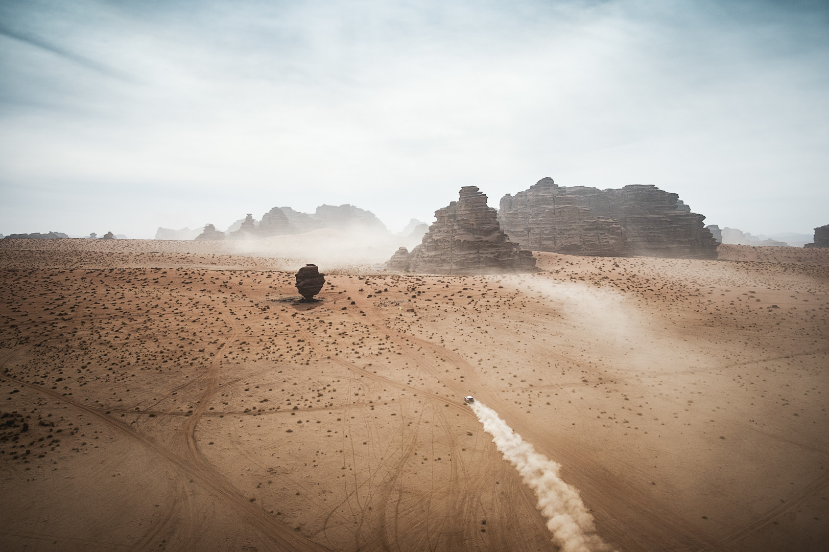 Aerial photograph of a rally car racing across a desert-like terrain in the Dakar Rally.