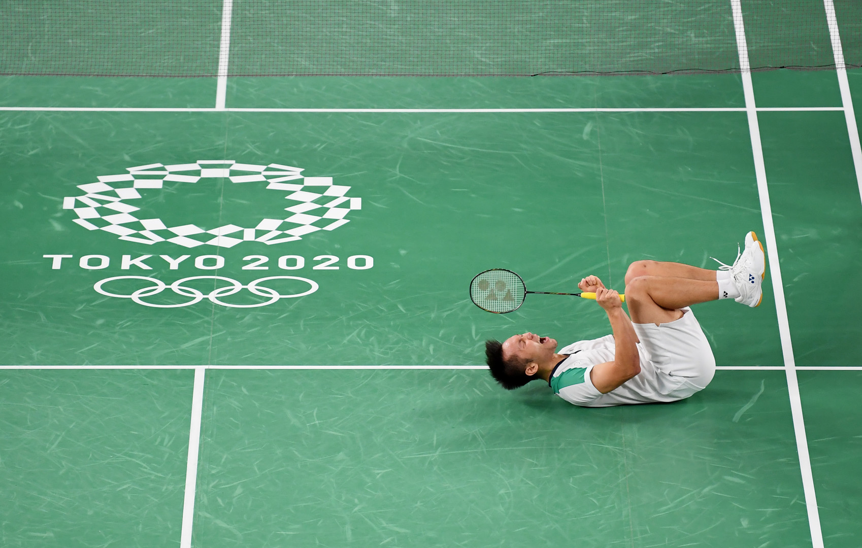 Male badminton player collapsed on green court floor in celebration as his wins.