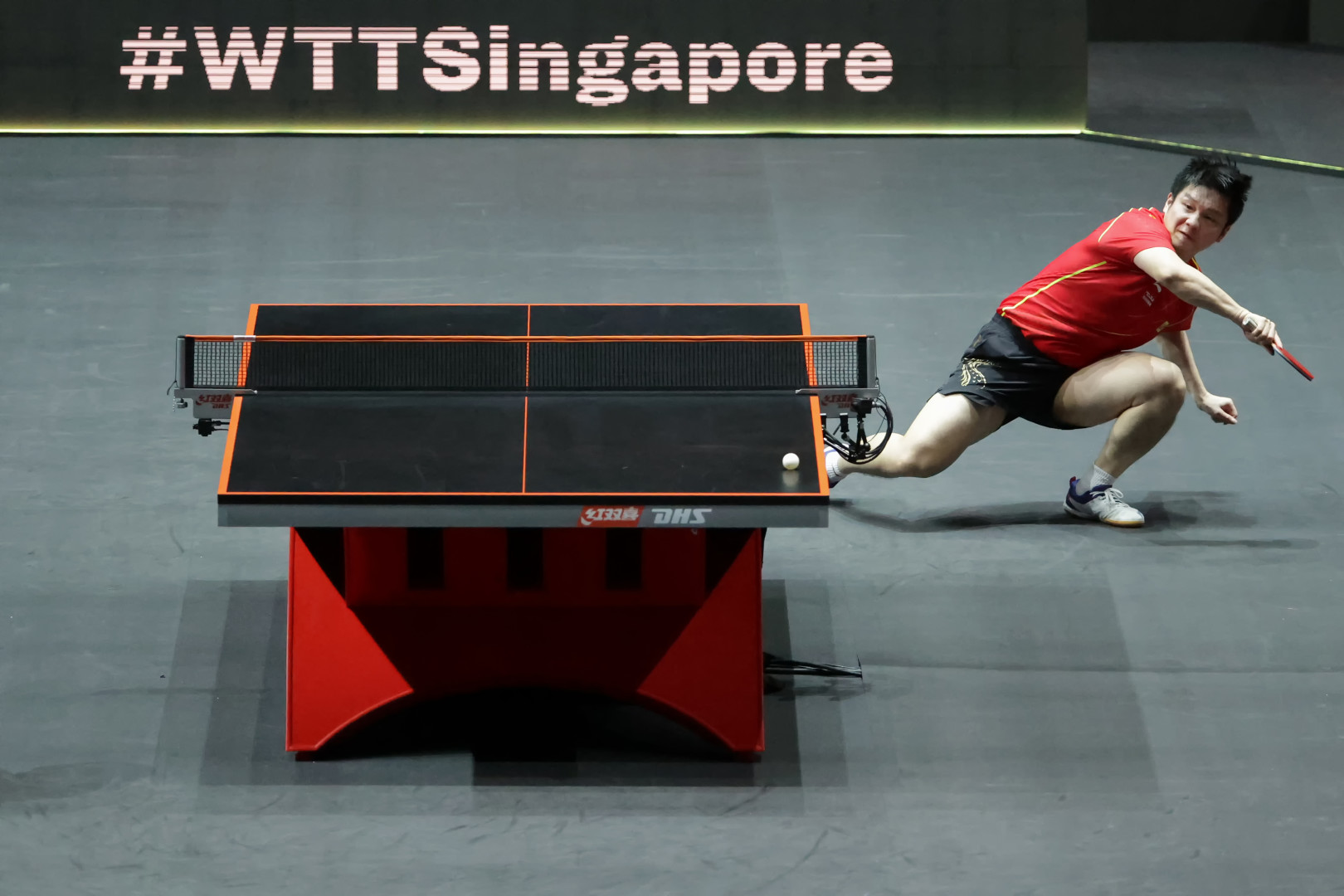 Table Tennis player falling, unbalance, to his left side as he hits a shot during a match at the Singapore WTT Cup finals.