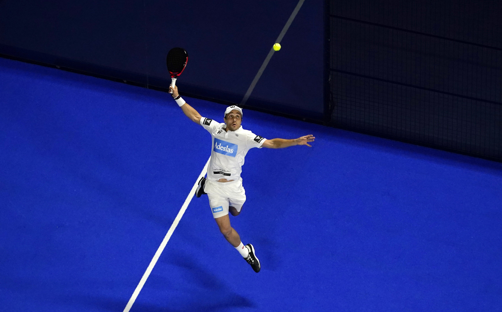 Fernando Belasteguín leaping up from a blue court to hit a shot with his padel at the World Padel Tour 2021.