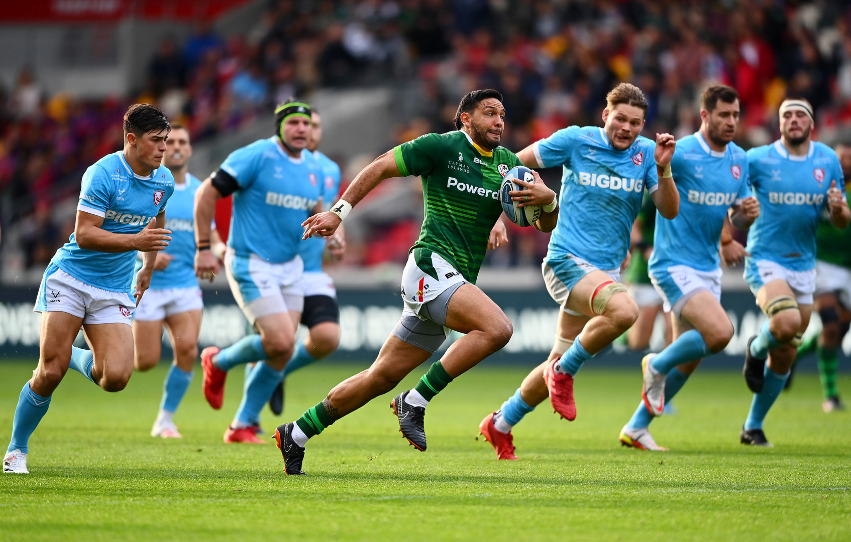 London Irish rugby player pacing down the pitch as he's chased by multiple Gloucester rugby players.