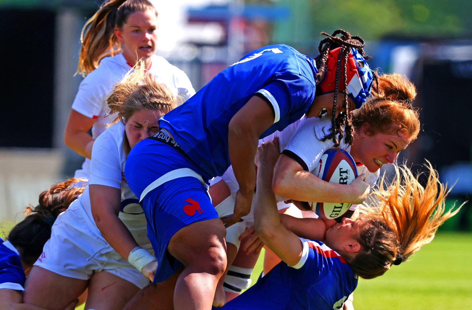 Multiple women's rugby players in a falling tackle for the rugby ball.