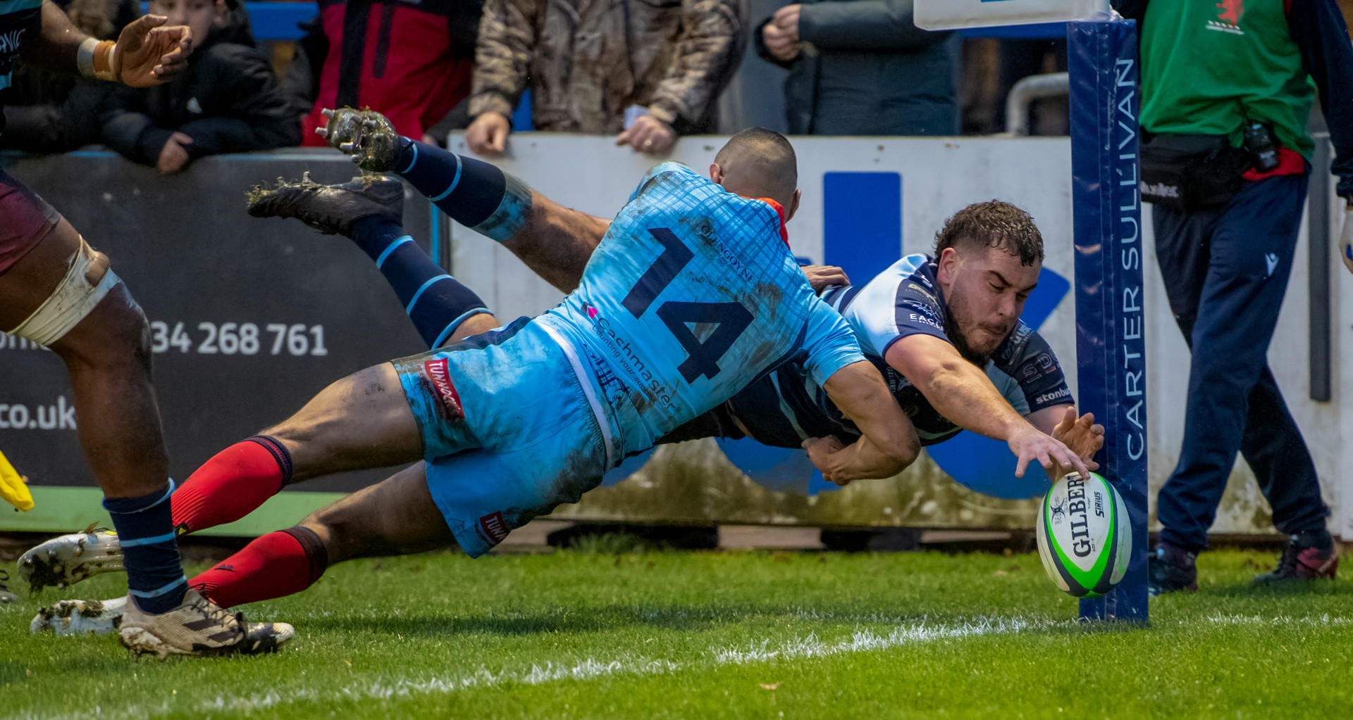 Jack Hughes of Bedford Blues being tackled off of the rugby pitch as he dives for a to make a try.