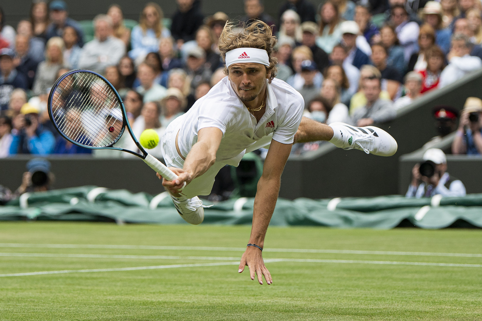 Tennis player launching himself across court to reach opposition players shot at the Wimbledon Tennis Championships.