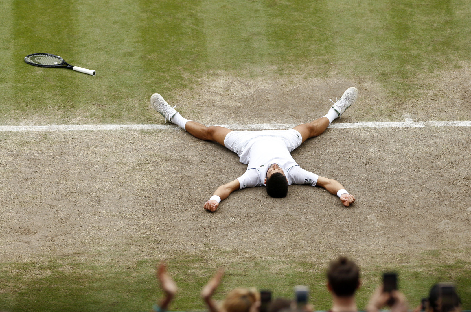 Novak Djokovic lying in a starfish position on the Wimbledon court as he wins the competition.