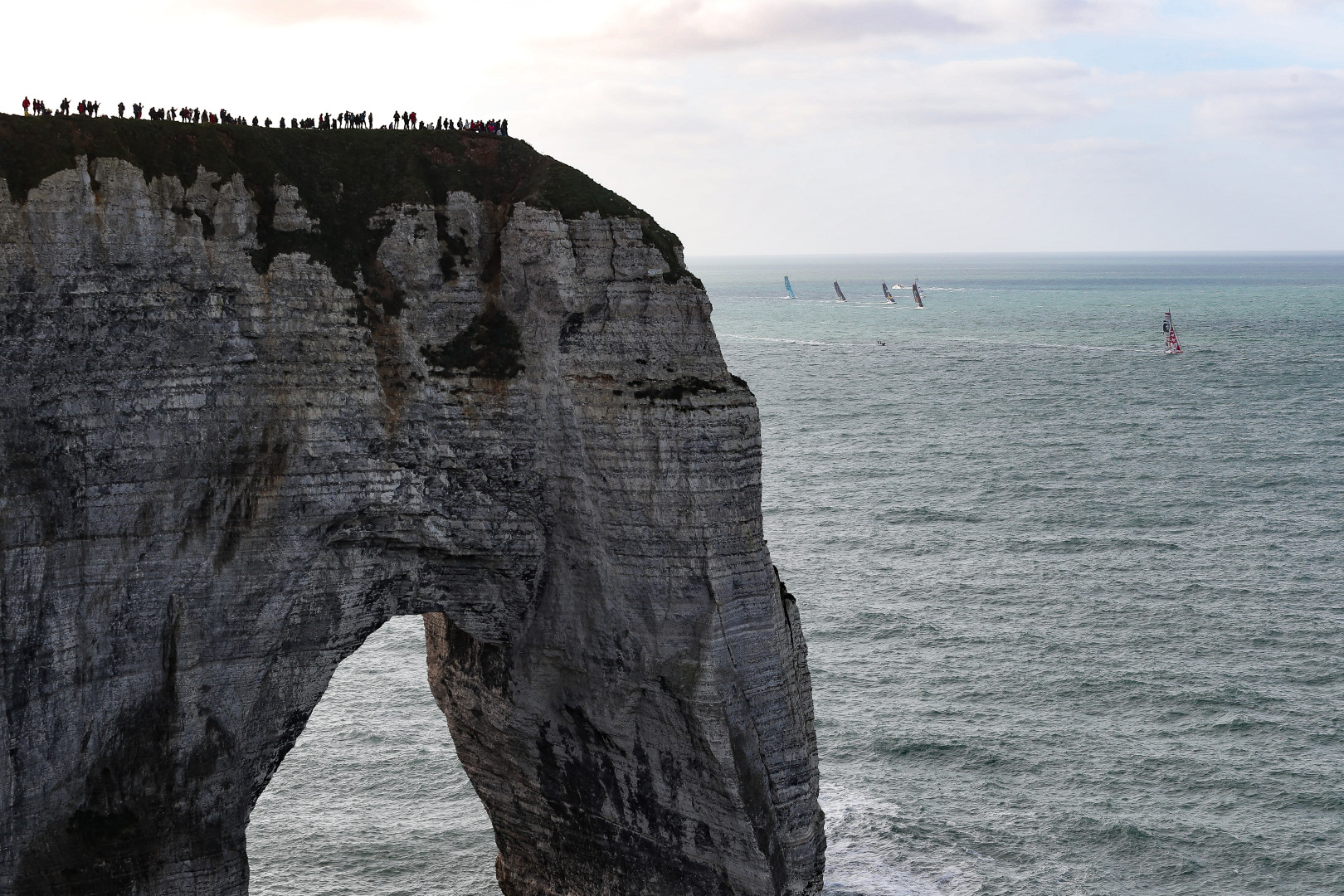 Ant sized people standing on top of Durdle Door watching a sailing competition.