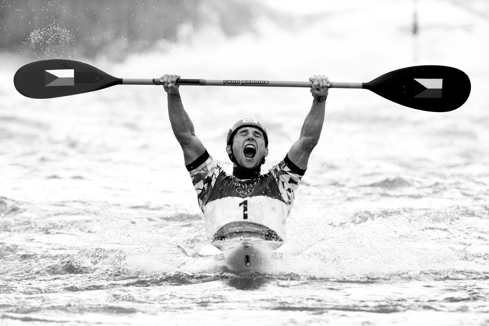 Black & White photograph of Slalom Canoeist holding his paddle in the air whilst screaming in celebration.