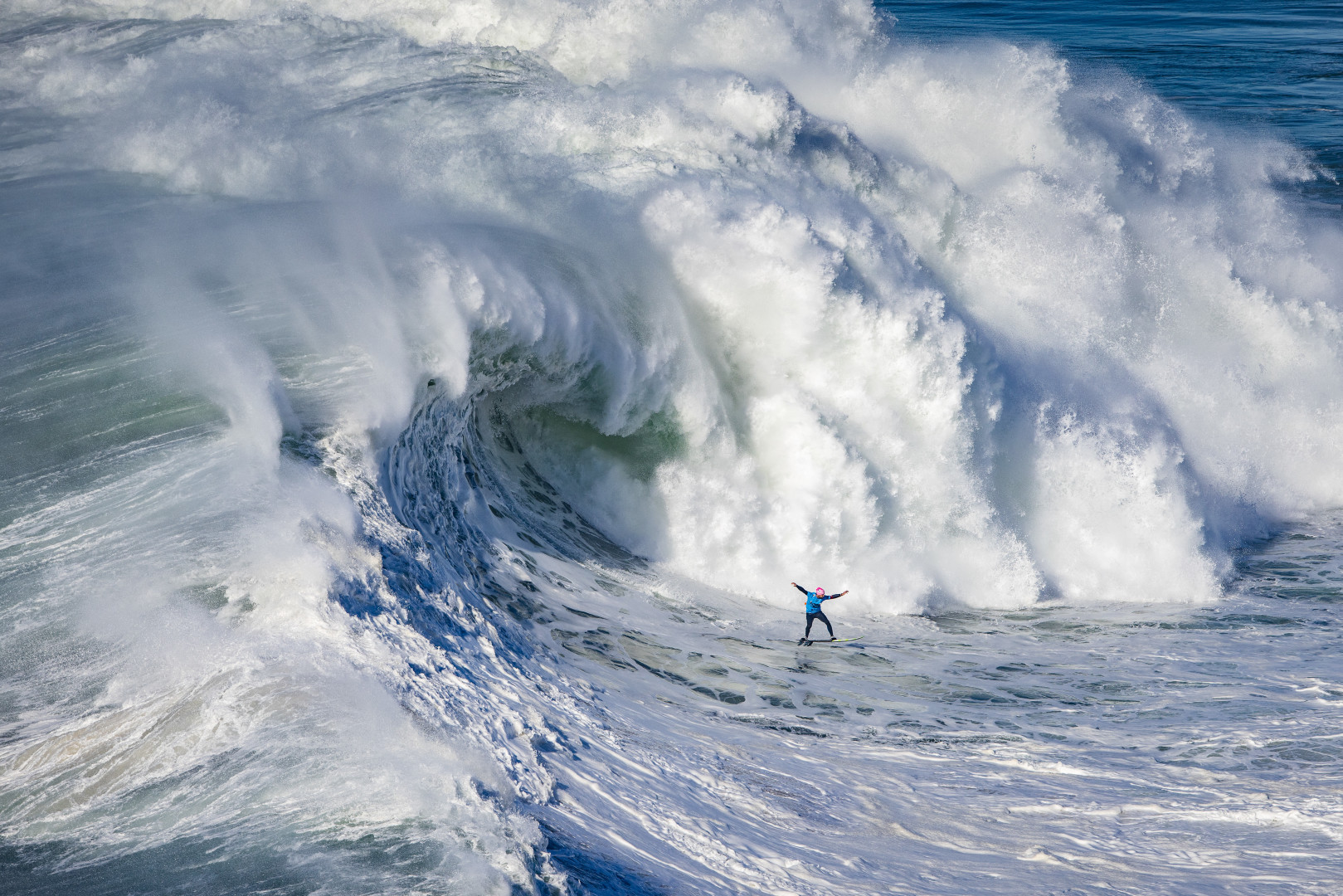 Tiny surfer being chased by a massive wave at the TUDOR Nazaré Tow Surfing Challenge.