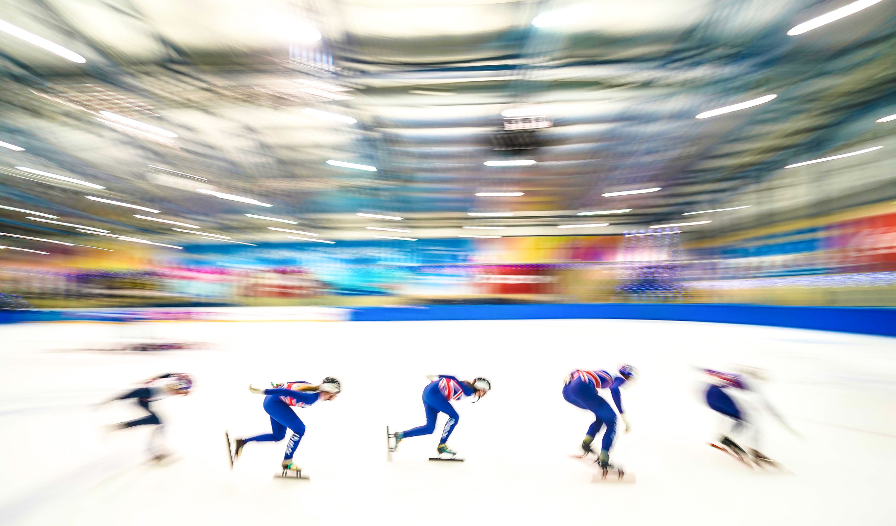 British ice racing team skating around indoor circuit in a blur of motion and colour.