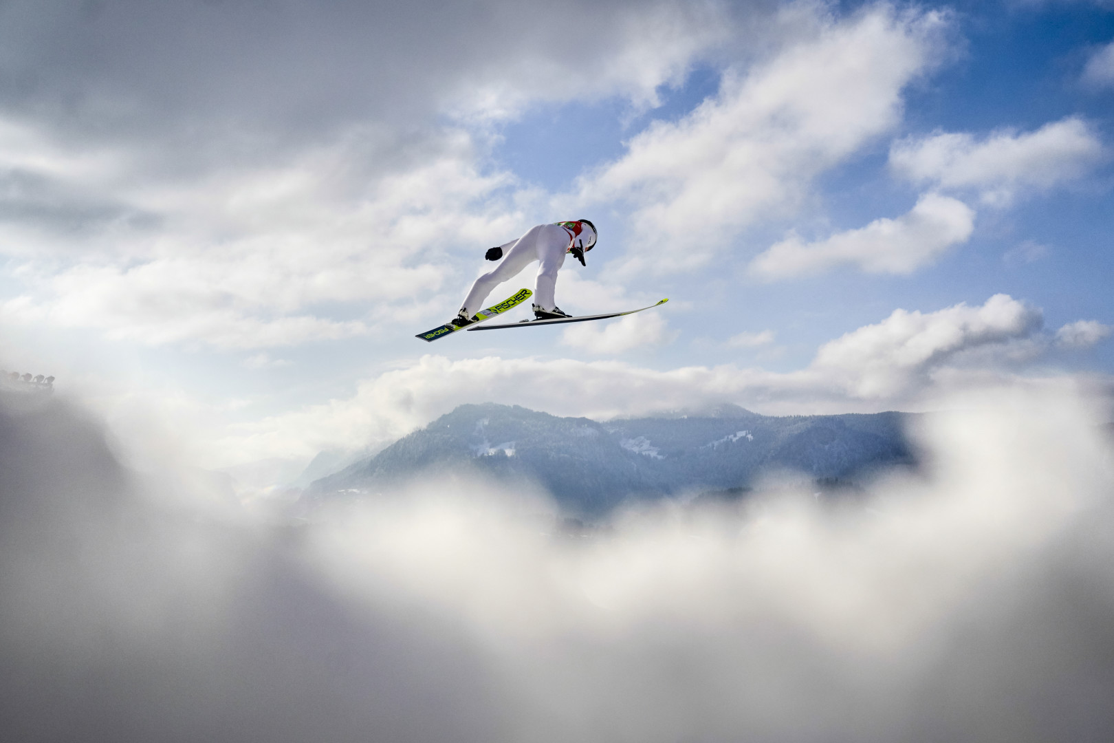 Ski jumper mid air as they travel through the clouds.