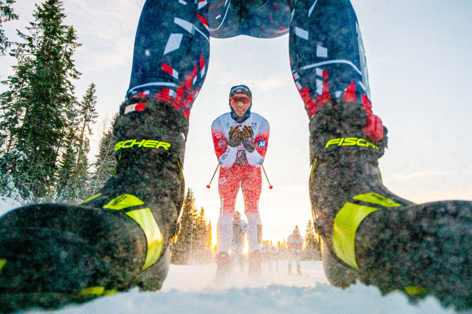 Photograph of a cross-country skier through the legs of another competitor.